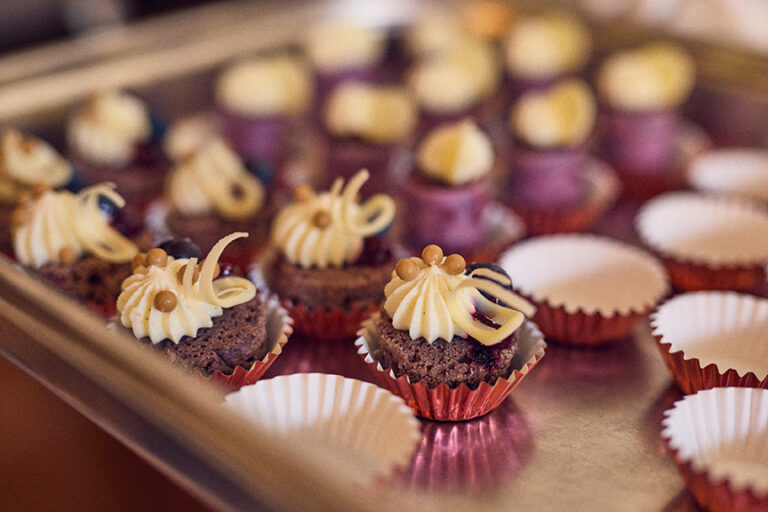 Mini-Schokoladen-Cupcakes mit Sahneglasur in roten Folienbechern, arrangiert auf einem Metalltablett - eine unwiderstehliche Leckerei, inspiriert von den süßen Momenten bei Philara 14 Places.