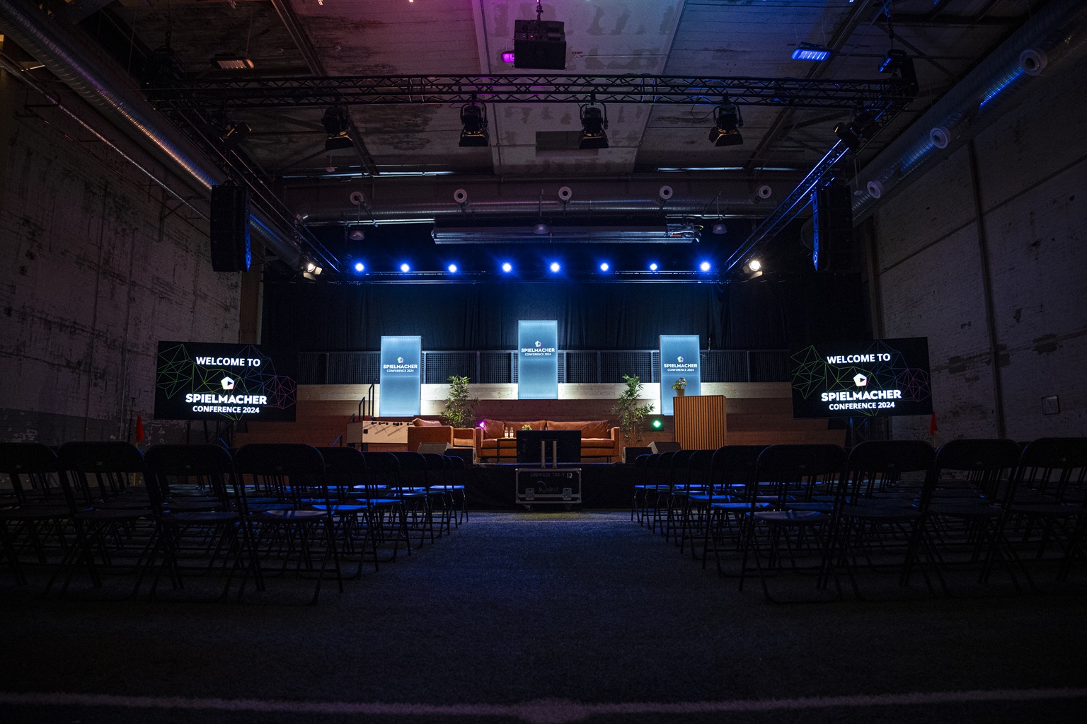 Ein Bühnenaufbau für die Spielmacher-Konferenz 2018 mit leeren Stühlen und blauer Beleuchtung.